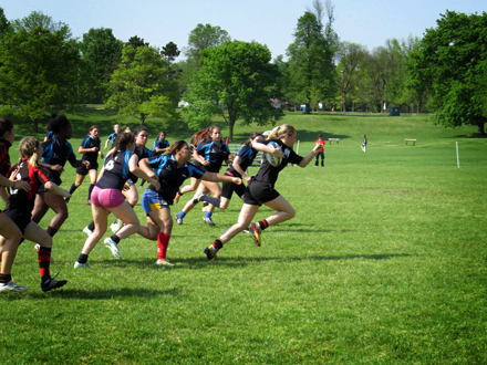 A girl breaks free from the pack in the rugby game trying to score in the end zone.
