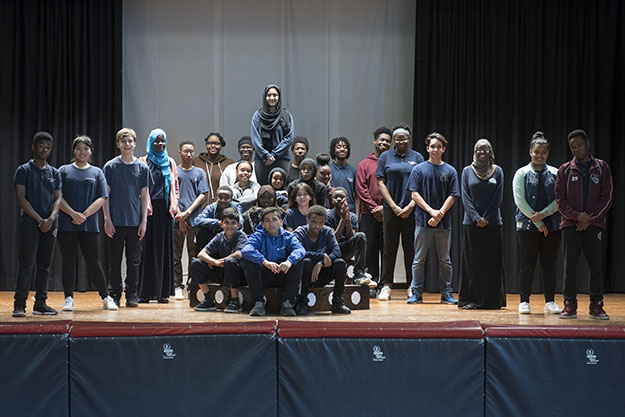 The student cast of 27 students poses for the camera on the school’s stage.
