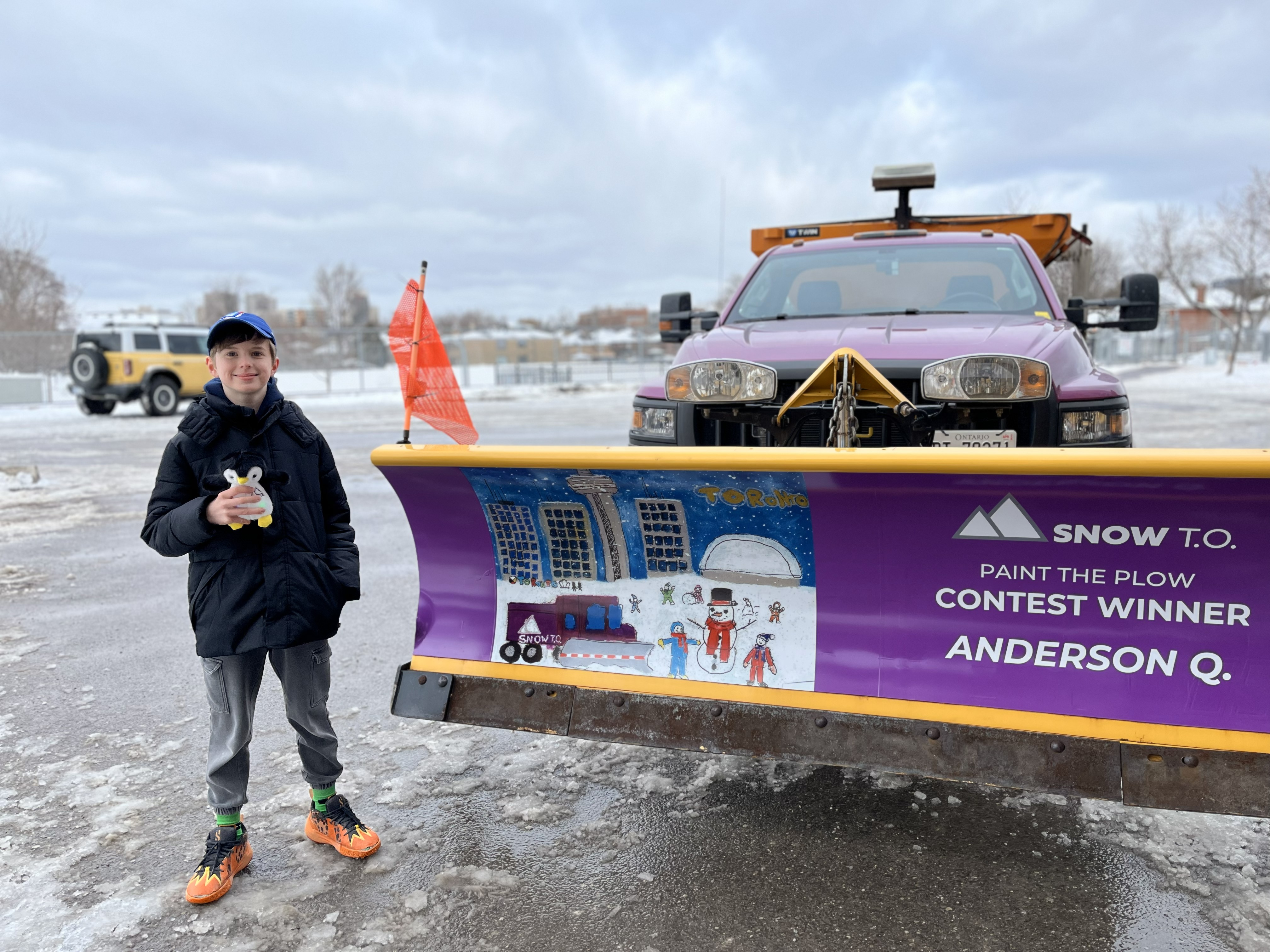 Student stands beside a snow plough decorated with their design of Toronto in winter 
