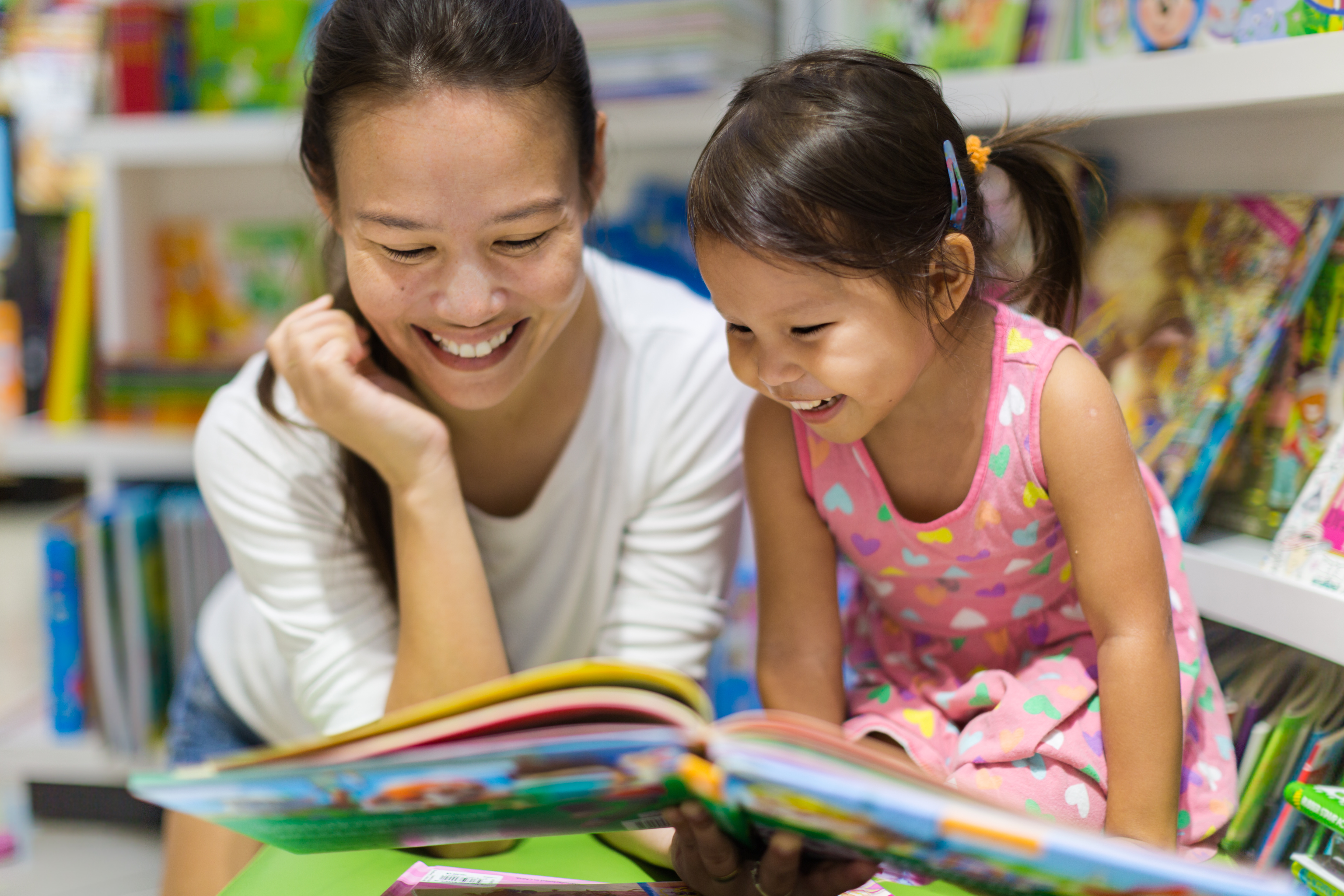 A pair of young child students pick out books from a classroom bookshelf