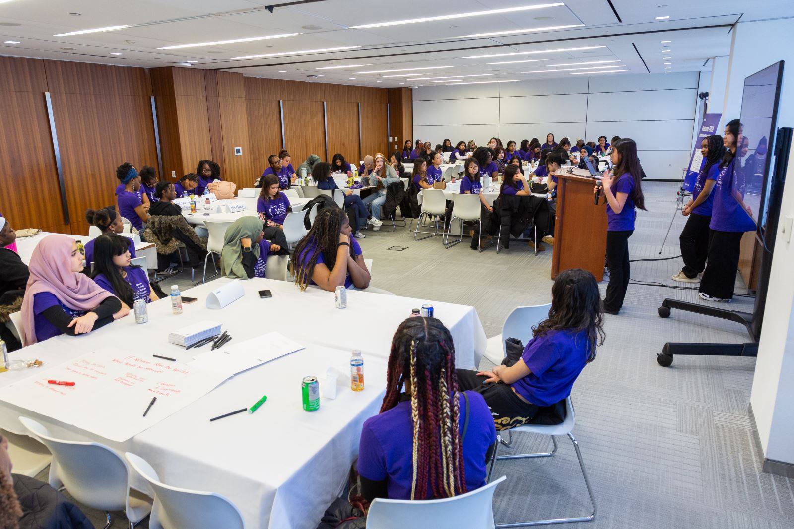 students seated in tables listening to student presentation
