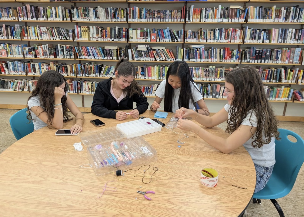Four individuals seated around a circular wooden table in a library, engaged in crafting activities.