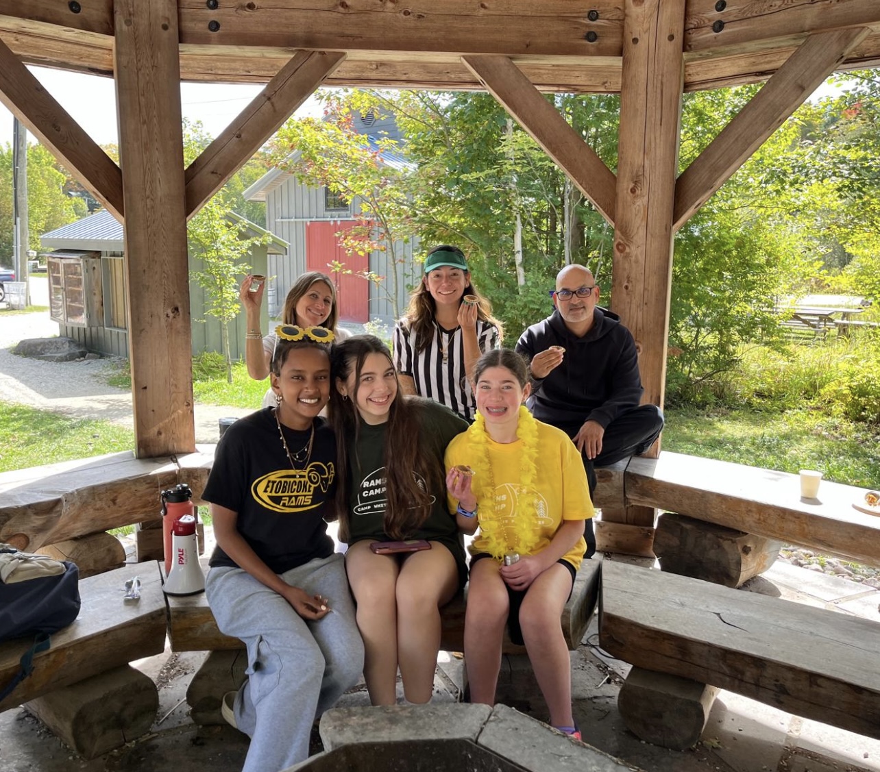 A group of six people sitting and standing under a wooden gazebo.