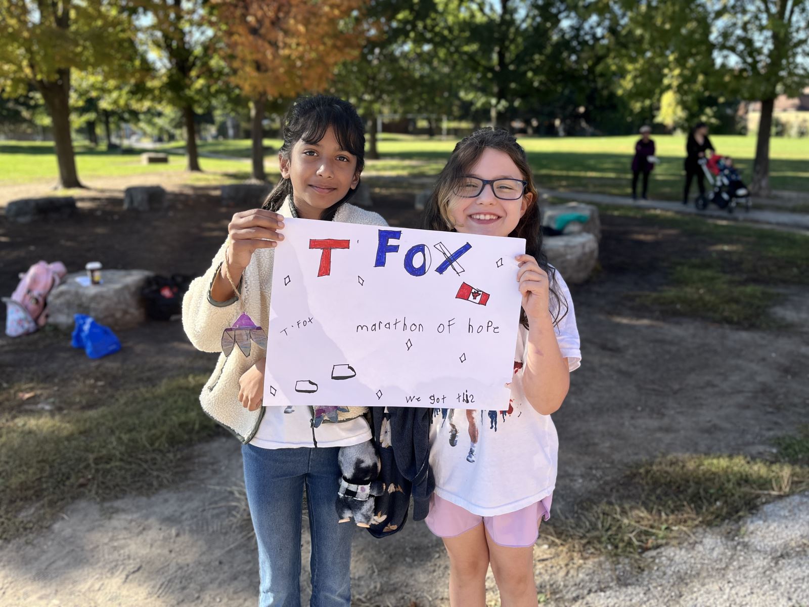 Two children standing outdoors in a park holding a handmade sign.