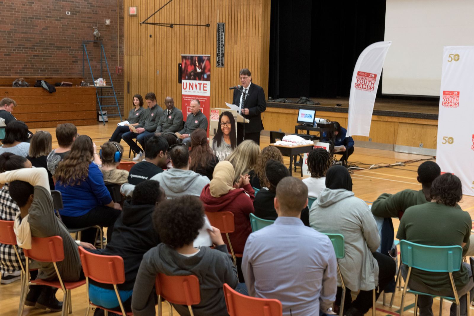 Trustee MacLean welcoming seated guests at an assembly for the Invitational Youth Games