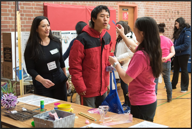 A participant of the fair being instructed to blow bubbles as a self-regulation strategy at TDSB's occupational therapy and physiotherapy services' booth at TDSB's planning for adulthood for students with disabilities transition fair