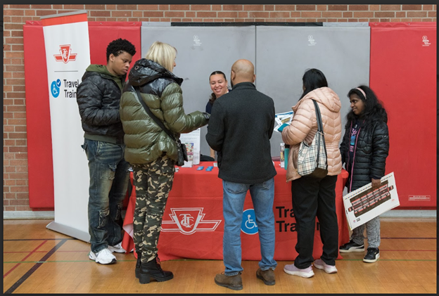A group of people gathered at the TTC transit training booth at TDSB's planning for adulthood for students with disabilities transition fair gathering information