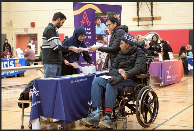 A family with a person in a wheelchair at the South Asian Autism Awareness Centre booth receiving information at TDSB's planning for adulthood for students with disabilities transition fair