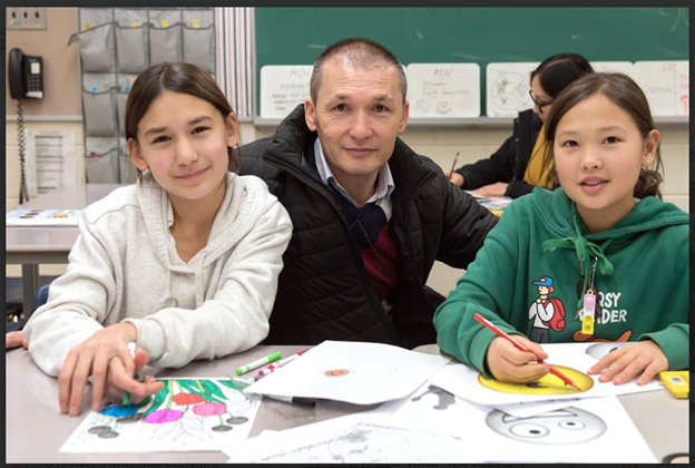 A person and two girls of a family sitting at a table colouring at one of the interactive stations at TDSB's planning for adulthood for students with disabilities' transition fair