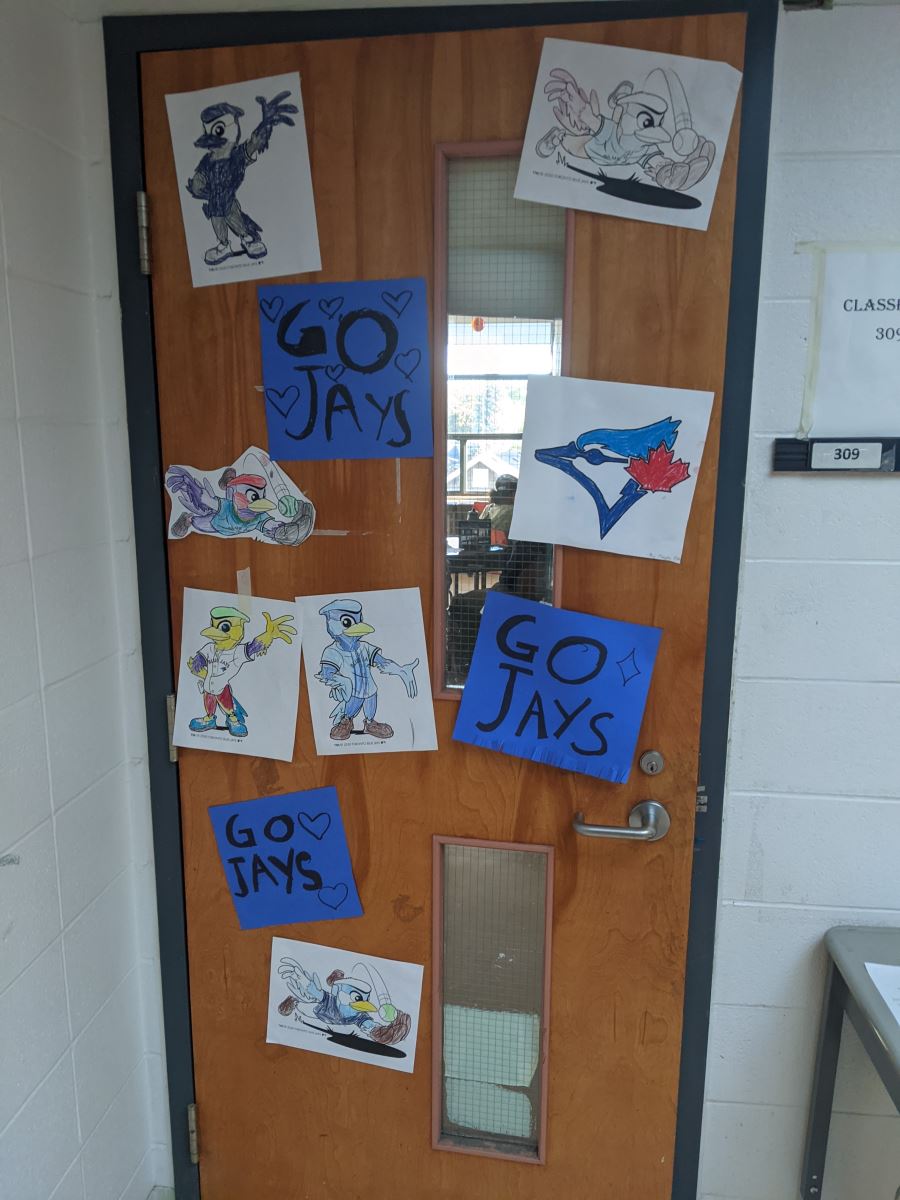 A school classroom door decorated with children's artwork and Blue Jays and logos and signs reading "Go Jays"