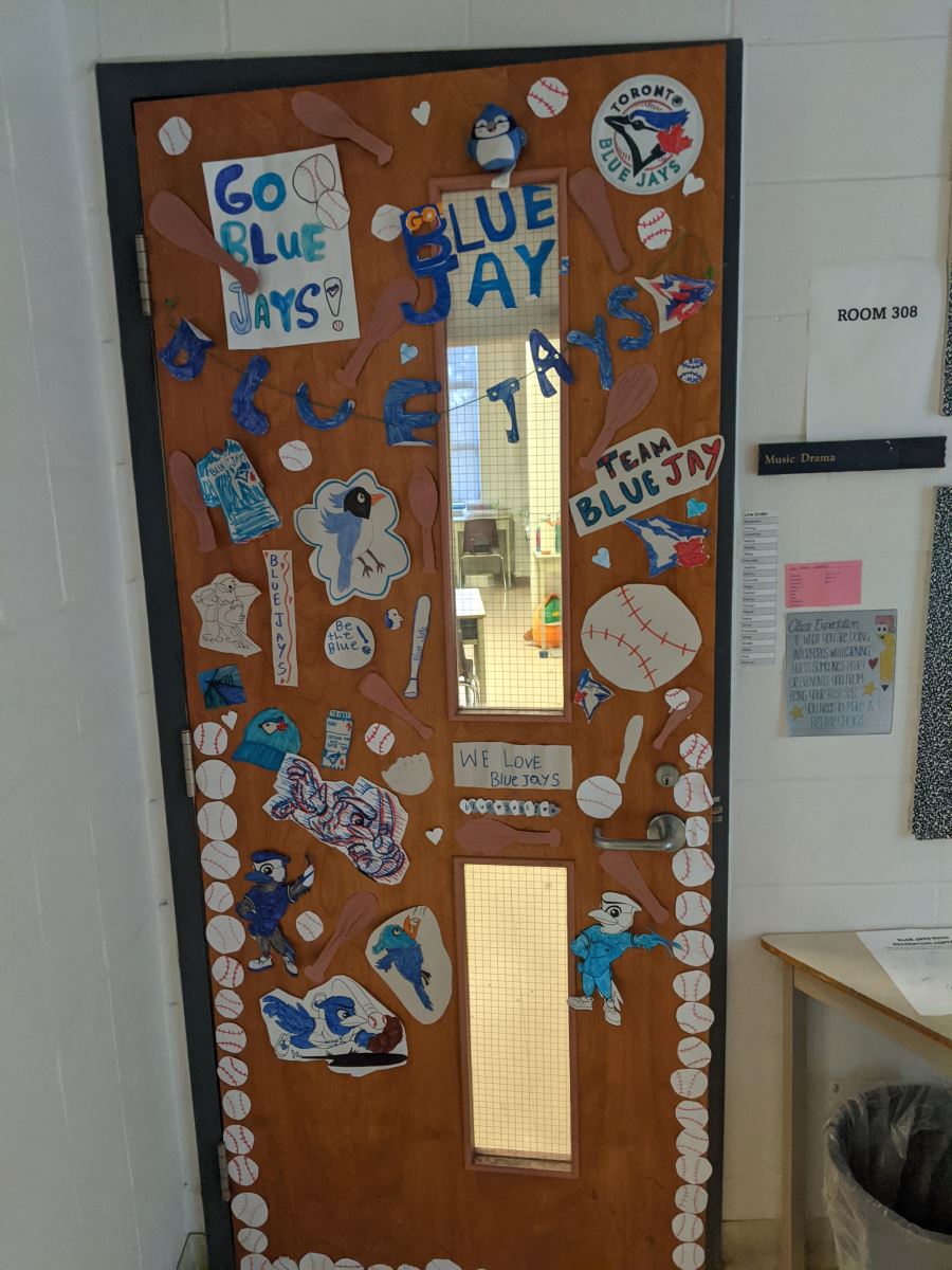 A school classroom door decorated with cut outs of baseballs and children's posters reading "Go Blue Jays"