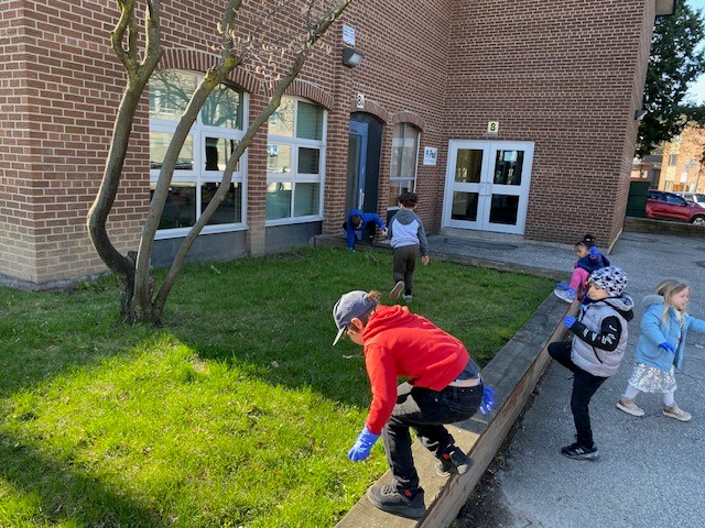 Students spread out across grass in front of a school picking up litter.