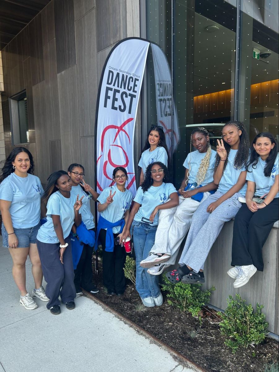 Students stand posing in a group in front of DanceFest signage