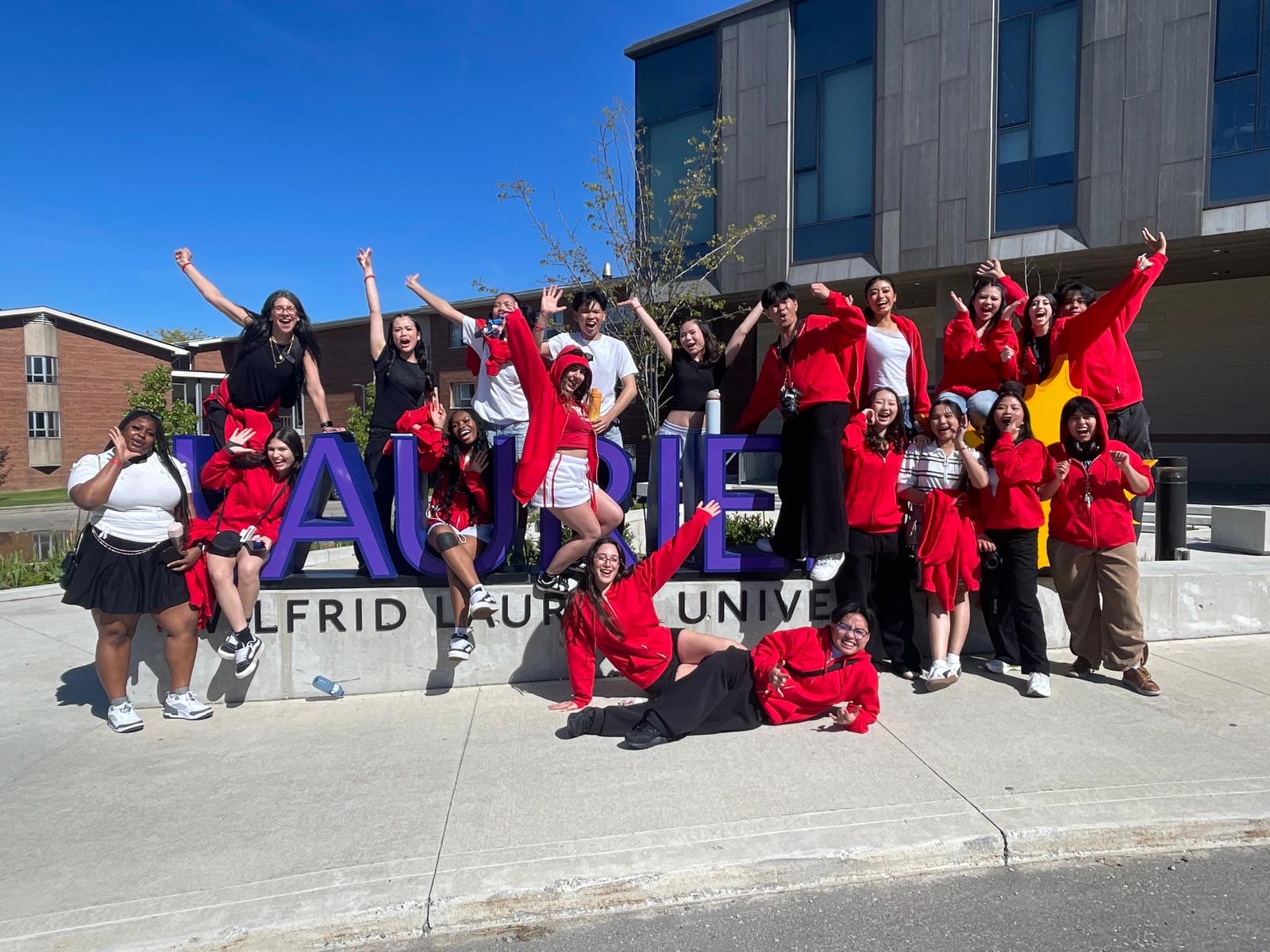 A group of students stands posing around a large Laurier sign