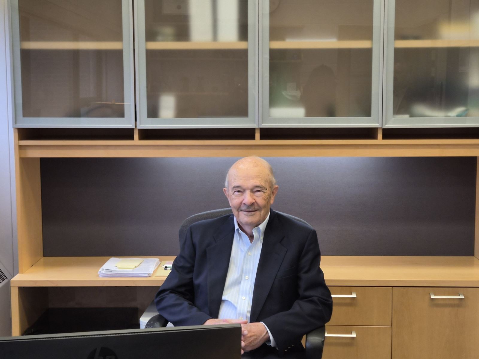 An individual seated at a desk in an office with wooden cabinetry and shelves, revisiting what appears to be a former workspace.