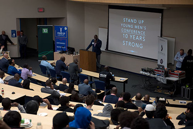 A Black mentor speaks in front of a crowd of students at the Stand Up Conference.