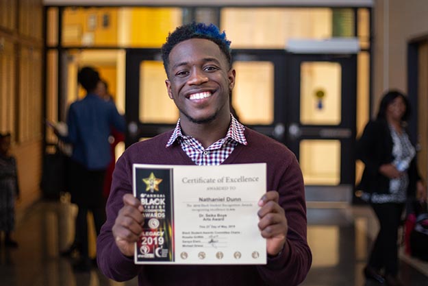 a Black male student holds up his certificate with pride.