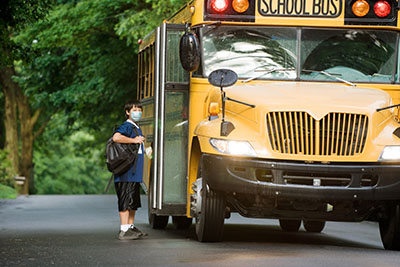 A student wearing a mask gets on a school bus