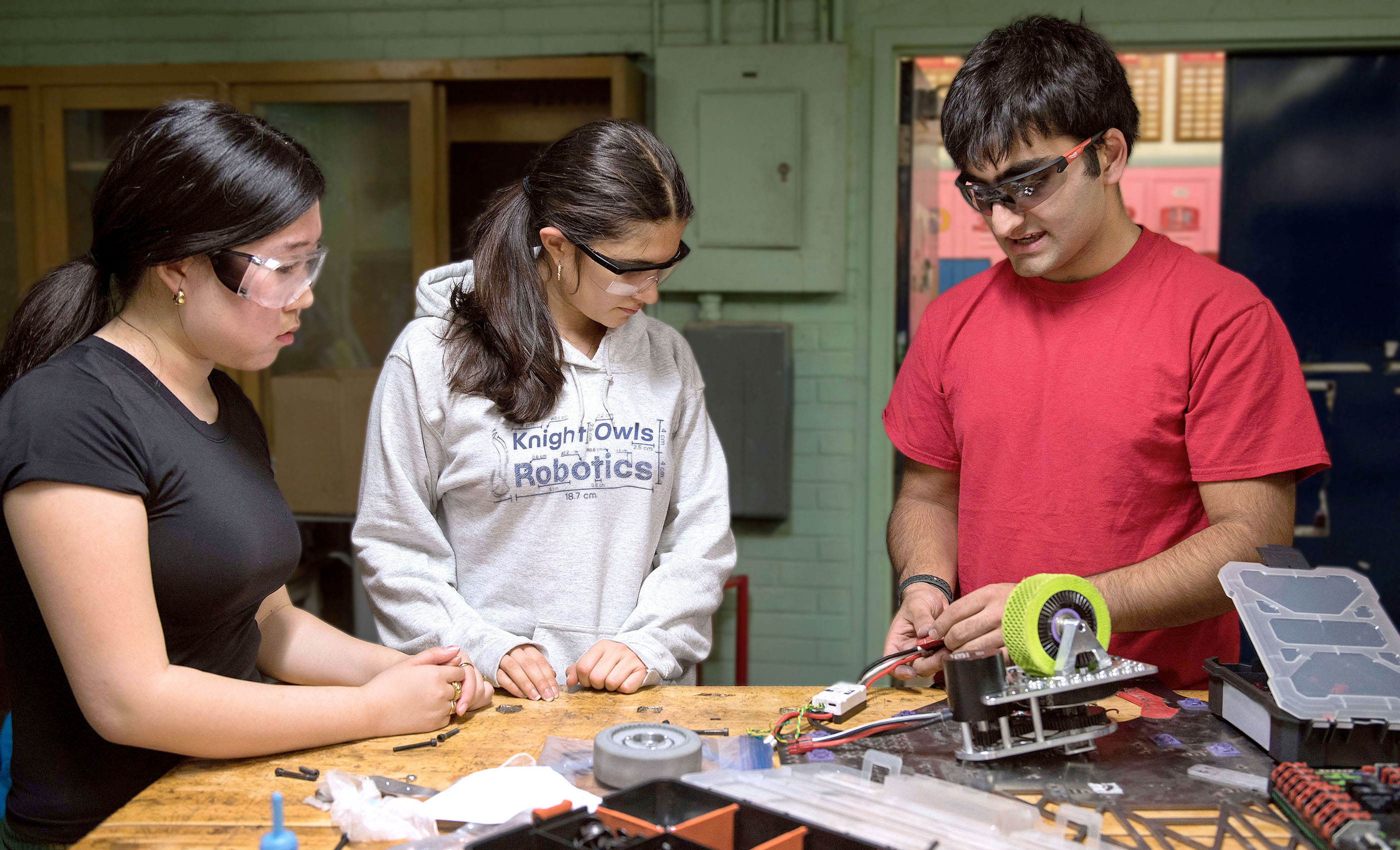 Three students wearing safety glasses working on robotics