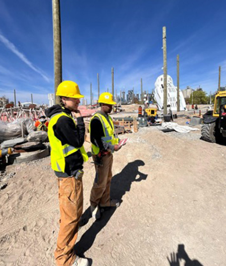 Two students in hard hats and vests standing in construction zone