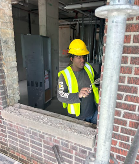 Student in hardhat and construction vest working with mortar