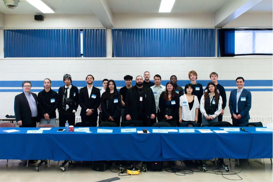 Students and instructors stand and pose behind long table