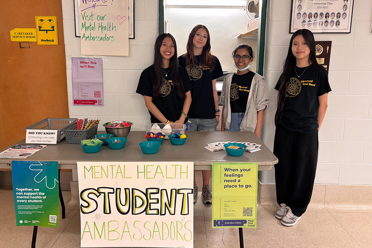 Four students standing behind a table with a sign that reads Menthal Health Student Ambassadors