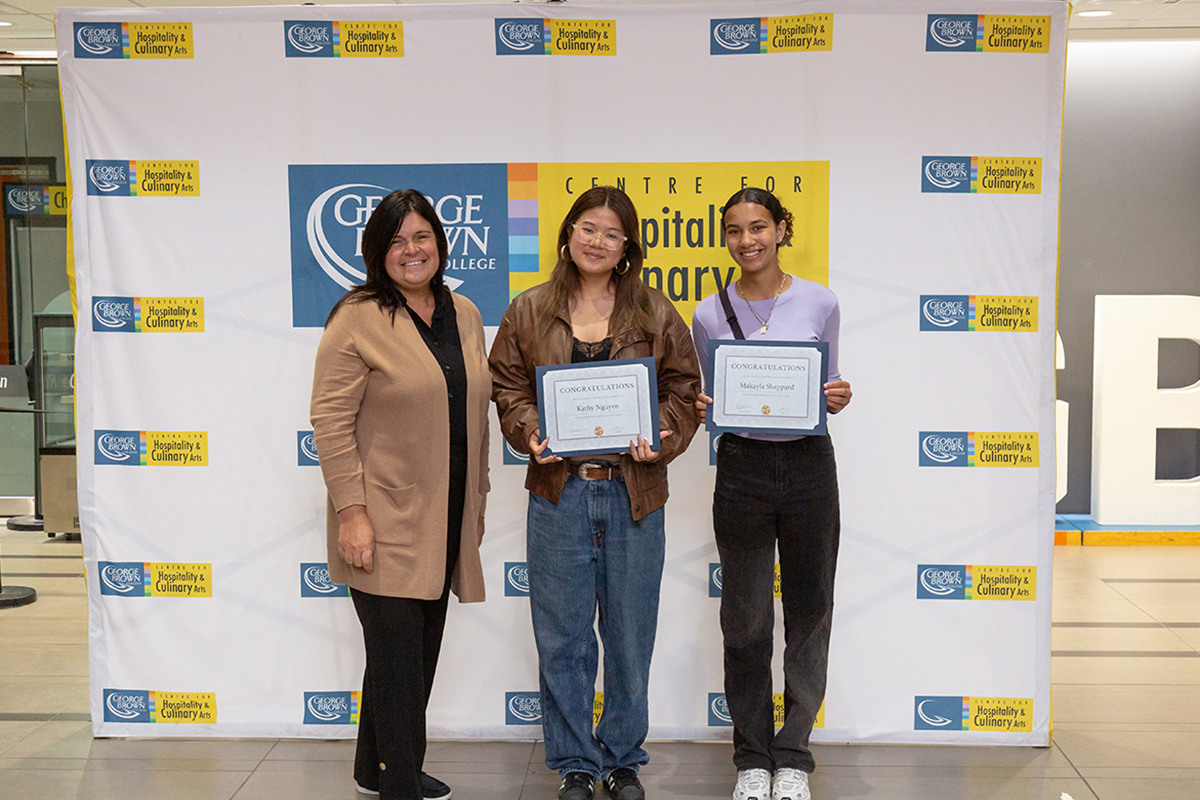 Educator stands with two students holding certificates